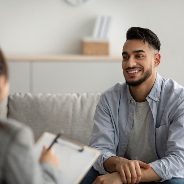 Effective psychotherapy. Happy middle eastern man talking to his psychologist, sharing therapy results with counselor, receiving professional help at mental health clinic